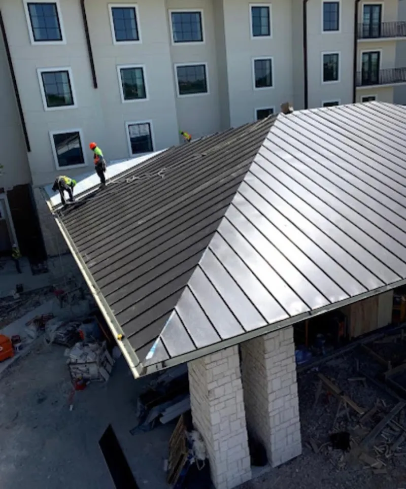 Crew installing standing seam metal roof panels on a commercial project in Elgin